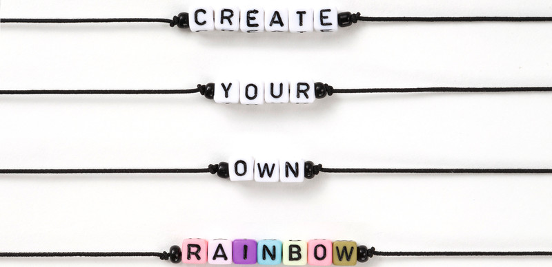 Beads on black cords spell out 'CREATE YOUR OWN RAINBOW' in uppercase letters.